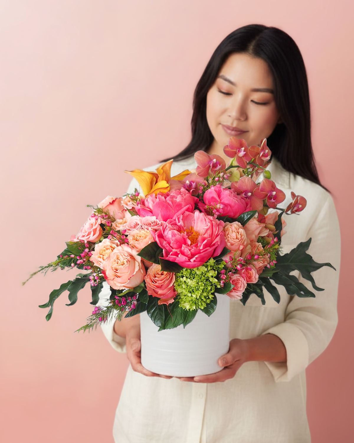 Woman holding a coral and peach modern flower arrangement against a light pink background